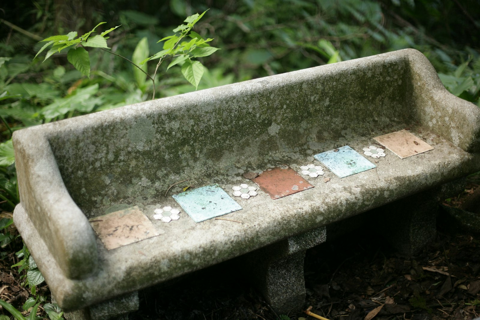 An old stone bench with decorative tiles in a garden.