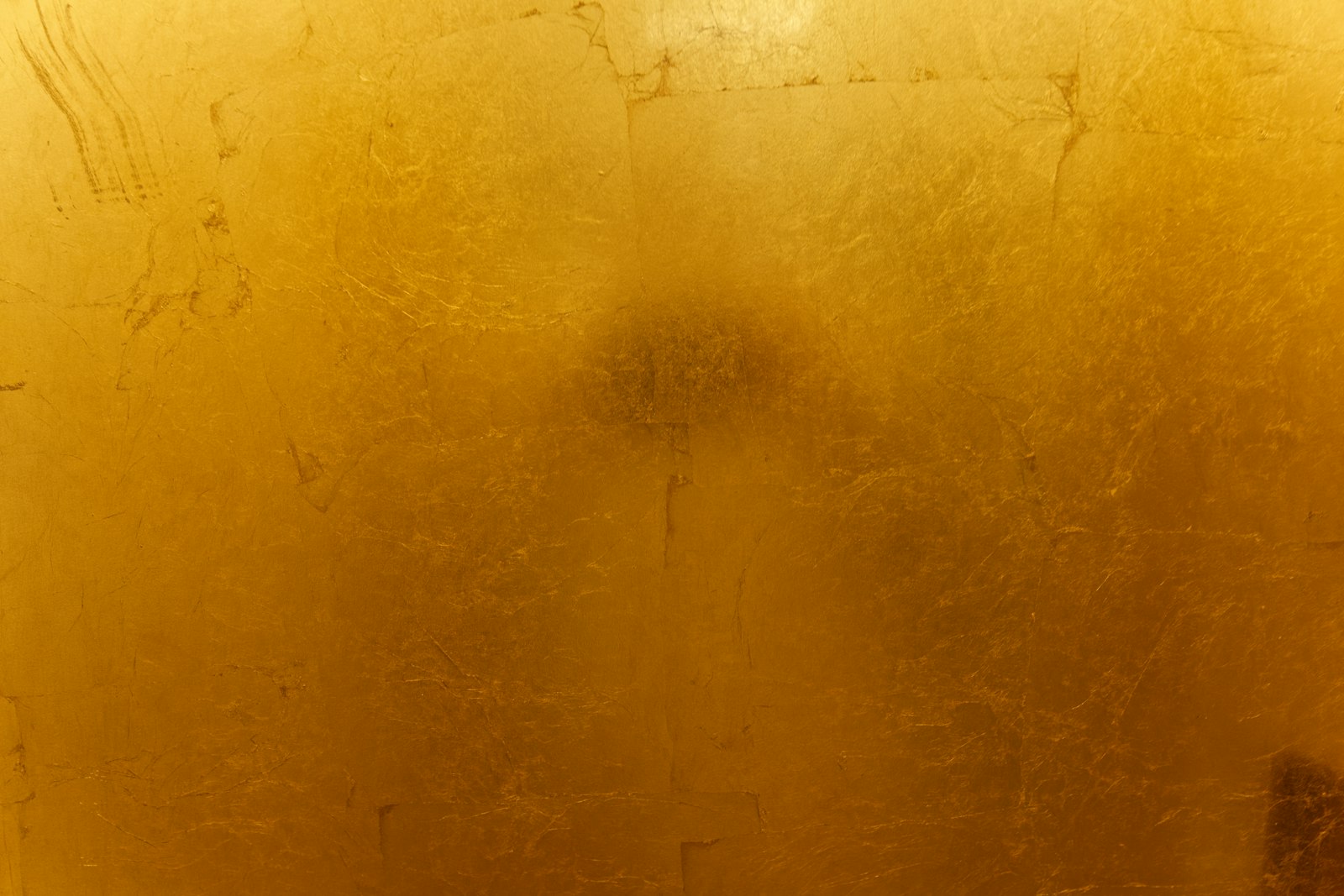 A textured gold leaf surface with visible overlapping seams and a soft shadow.